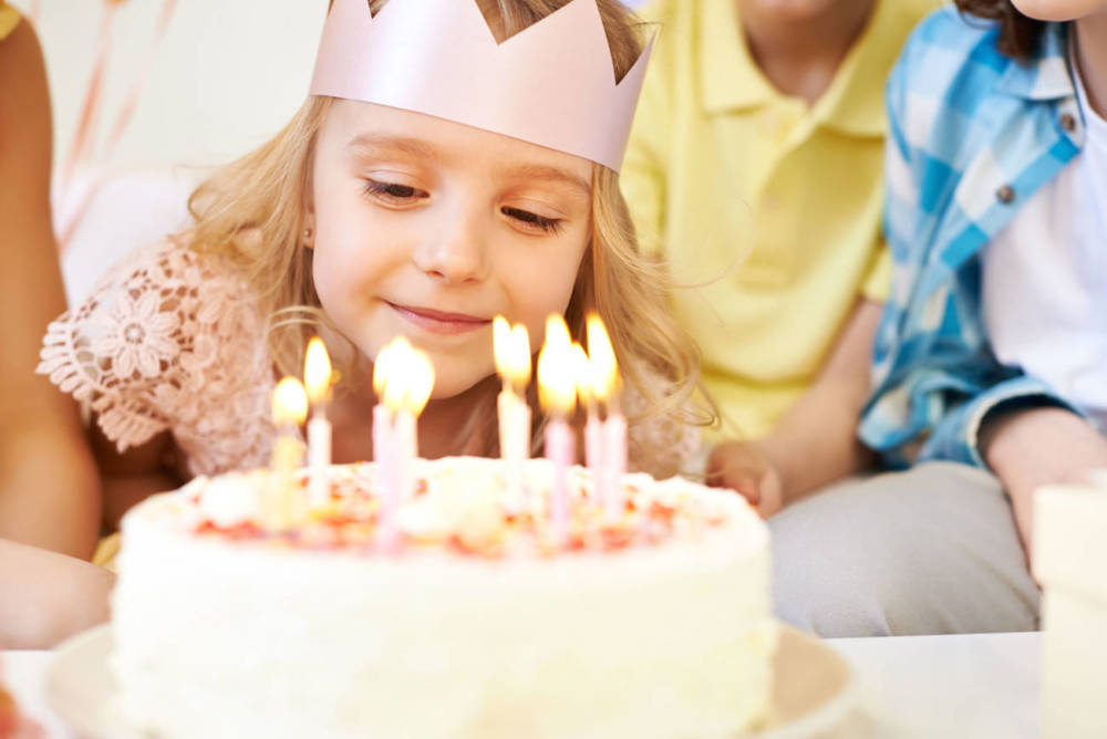 Girl with a pink crown made of paper bout to blow out candles on a cake