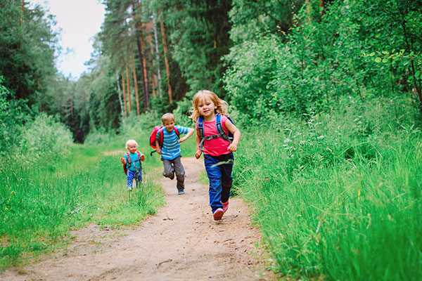3 kids running on trail in the middle of tall green trees