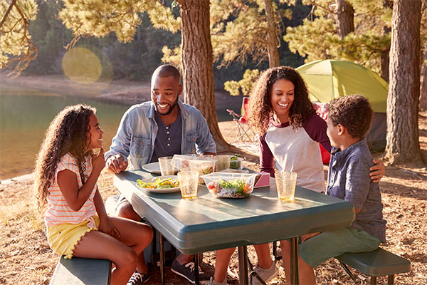 family of 4 sitting down for meal at a picnic table 