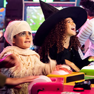 Two children in Halloween costumes playing a game. One child is dressed as a Halloween mummy and the other child is wearing a Halloween witch hat. 