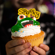 Two small hands holding a Halloween decorated vanilla cupcake.