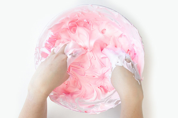 Two hands reaching in a bowl of pink slime. 