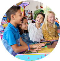 4 children laughing and cheering on friend as they play arcade game together