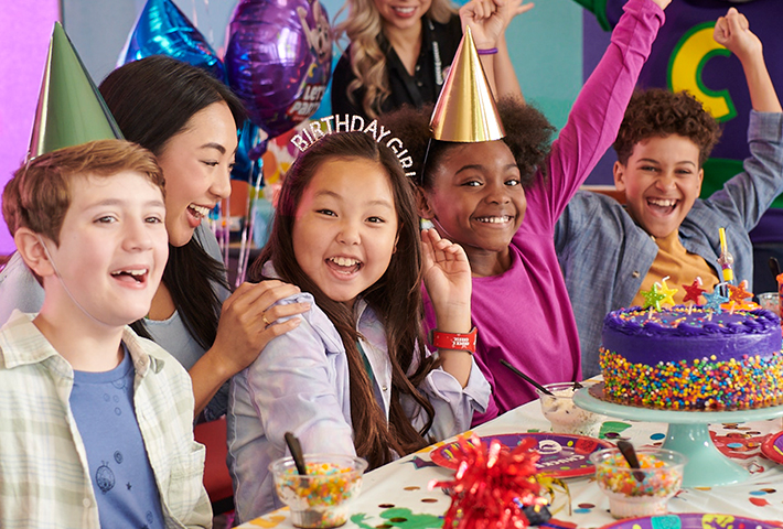 young girl celebrating birthday with purple cake and her friends