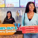 Lady carrying out tree Chuck E. Cheese pizzas boxes.