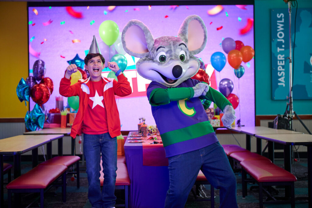 Boy and Chuck E. celebrating and dancing in front of birthday table.