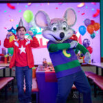 Boy and Chuck E. celebrating and dancing in front of birthday table.