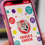 Person holding phone displaying Chuck E. Cheese website.