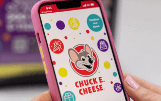 Person holding phone displaying Chuck E. Cheese website.
