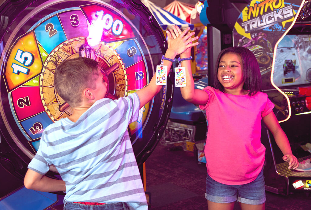 kids high fiving at chuck e cheese arcade with chuck e cheese play cards on their arms