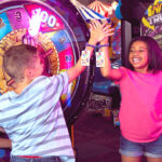 kids high fiving at chuck e cheese arcade with chuck e cheese play cards on their arms