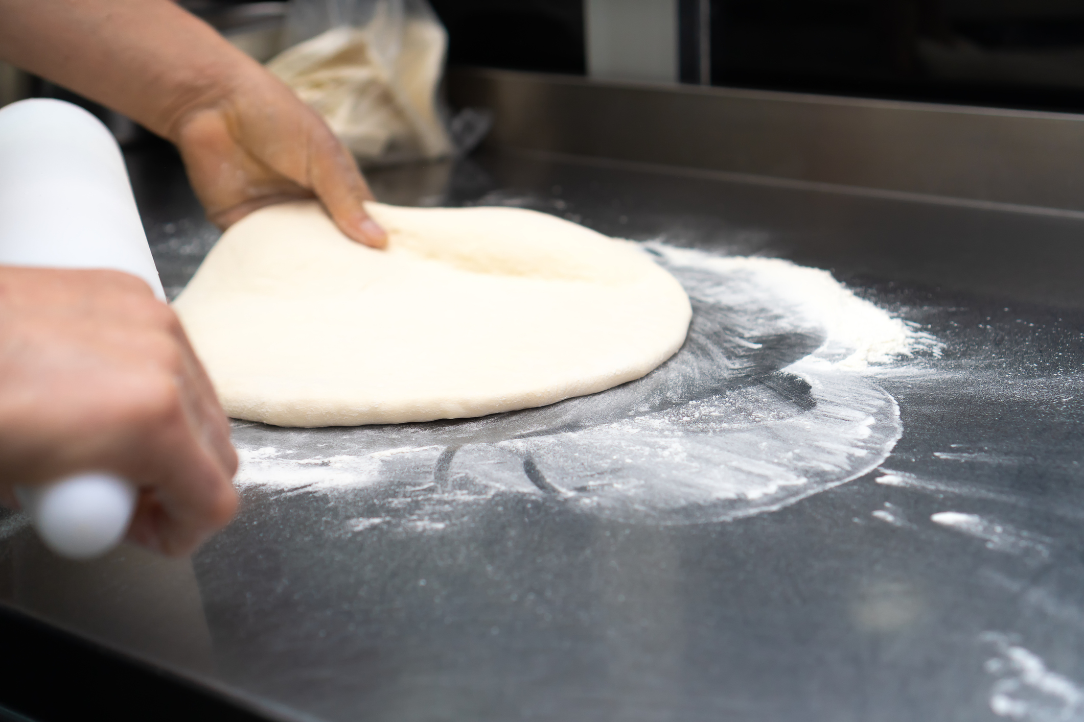 Hands stretching pizza dough on a floured counter at Chuck E. Cheese