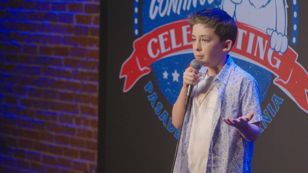 a young boy performing standup comedy in a stage holding a mic