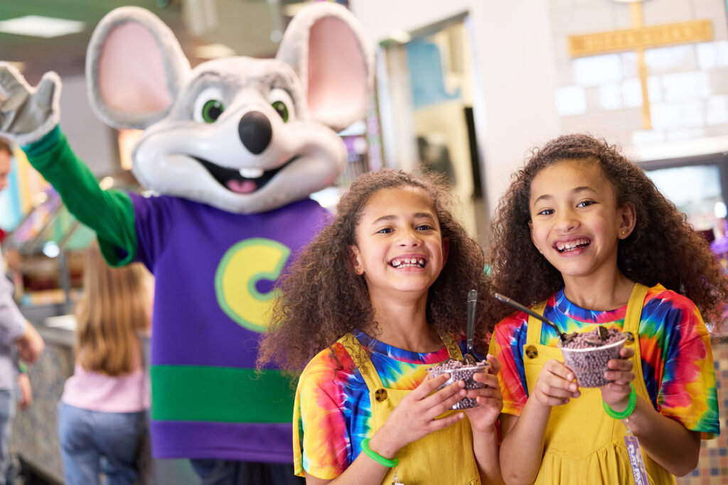 a group of girls holding cups with spoons and chuck e. cheese in the background