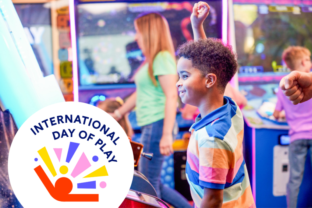young boy playing arcade game with international day of play logo on bottom left