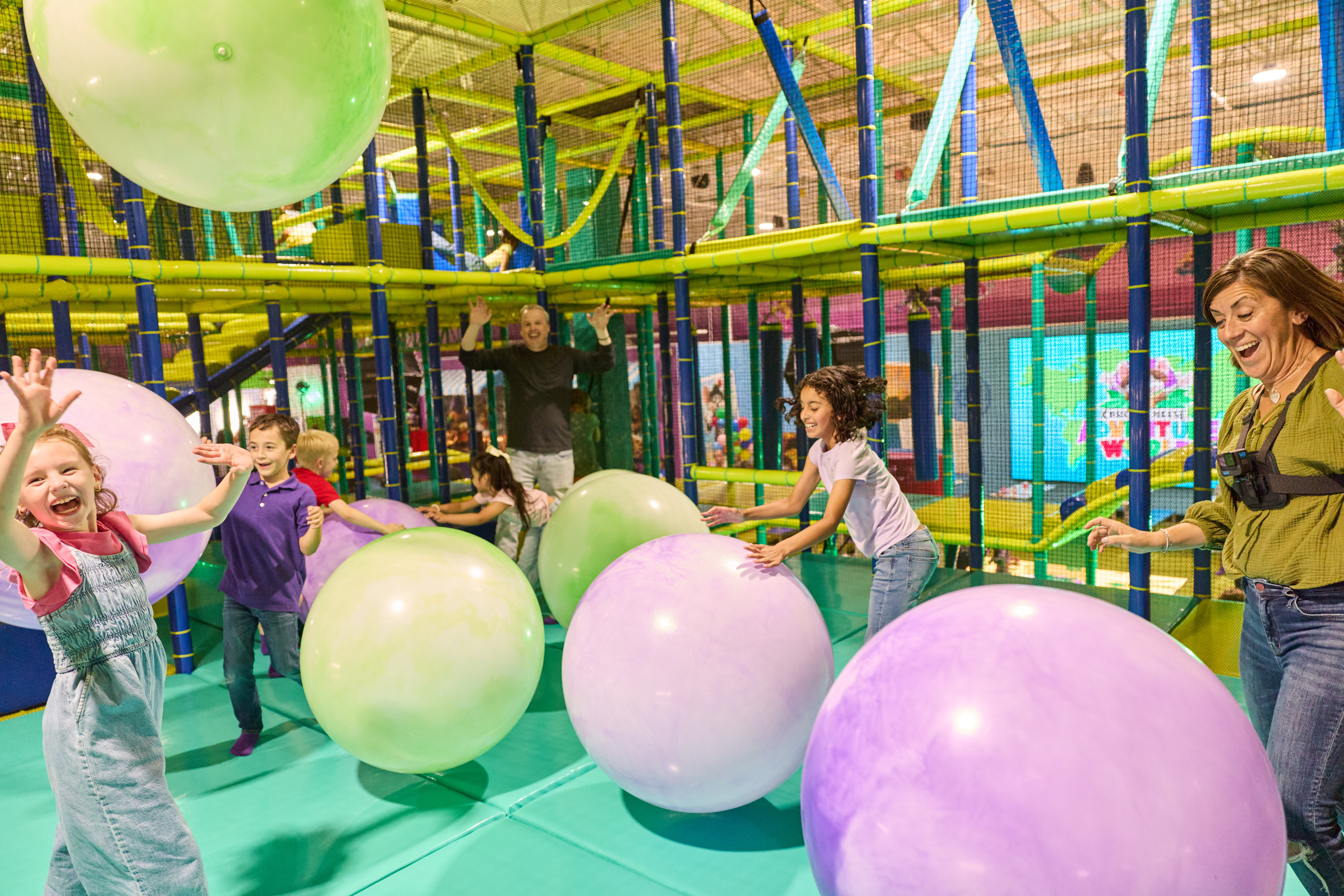 Kids play with pastel balls and climb in Chuck E. Cheese's indoor playground, surrounded by arcade games and birthday party fun.