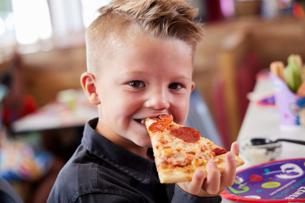 A young guest enjoying a slice of pepperoni pizza at Chuck E. Cheese.