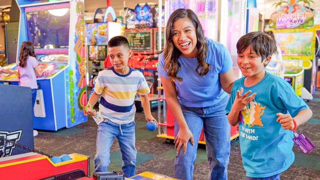 Mom and two kids laughing together at a Chuck E. Cheese arcade game