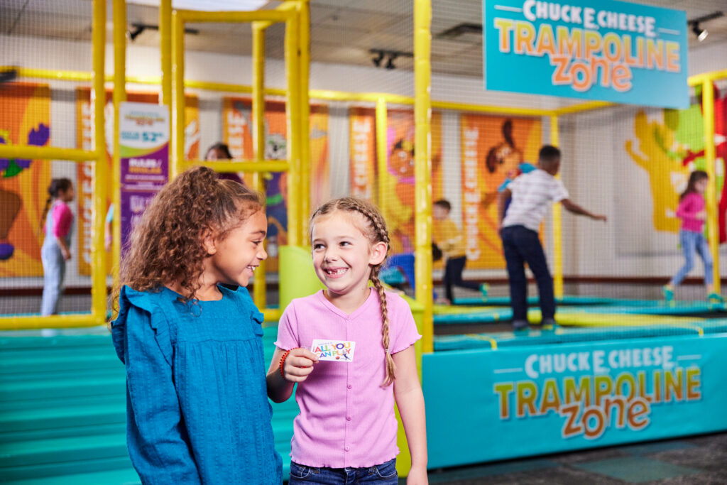Group of kids mid-jump on the enclosed Trampoline Zone at Chuck&nbsp;E.&nbsp;Cheese, yellow safety netting visible