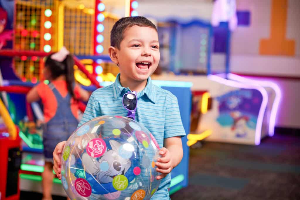Boy age 5–7 holds a colorful cartoon ball in Chuck E. Cheese arcade games area