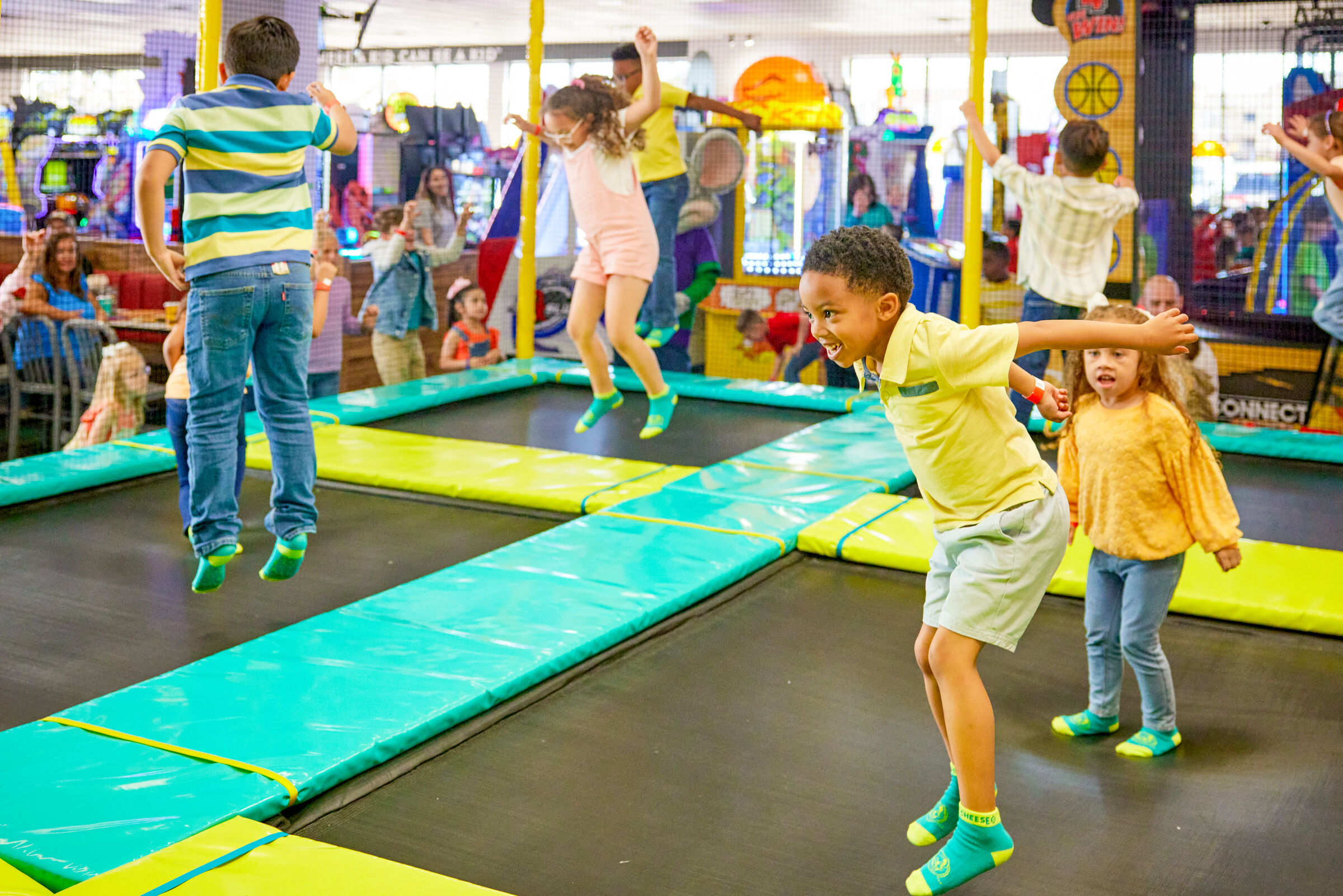 Kids jumping on indoor trampolines at Chuck E. Cheese near arcade games