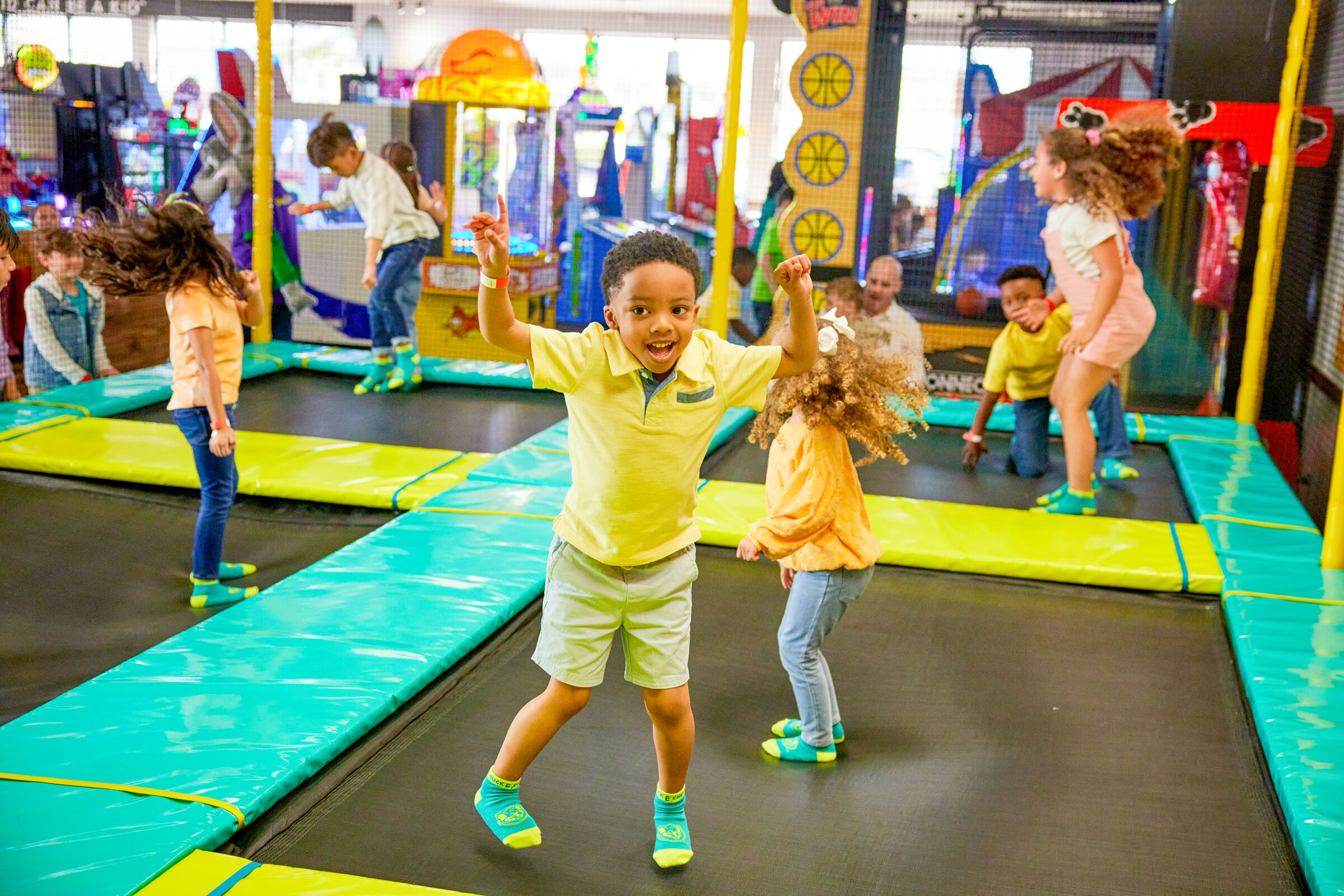 Kids jumping on trampolines at Chuck&nbsp;E.&nbsp;Cheese, with arcade games and colorful padded floors in the background.