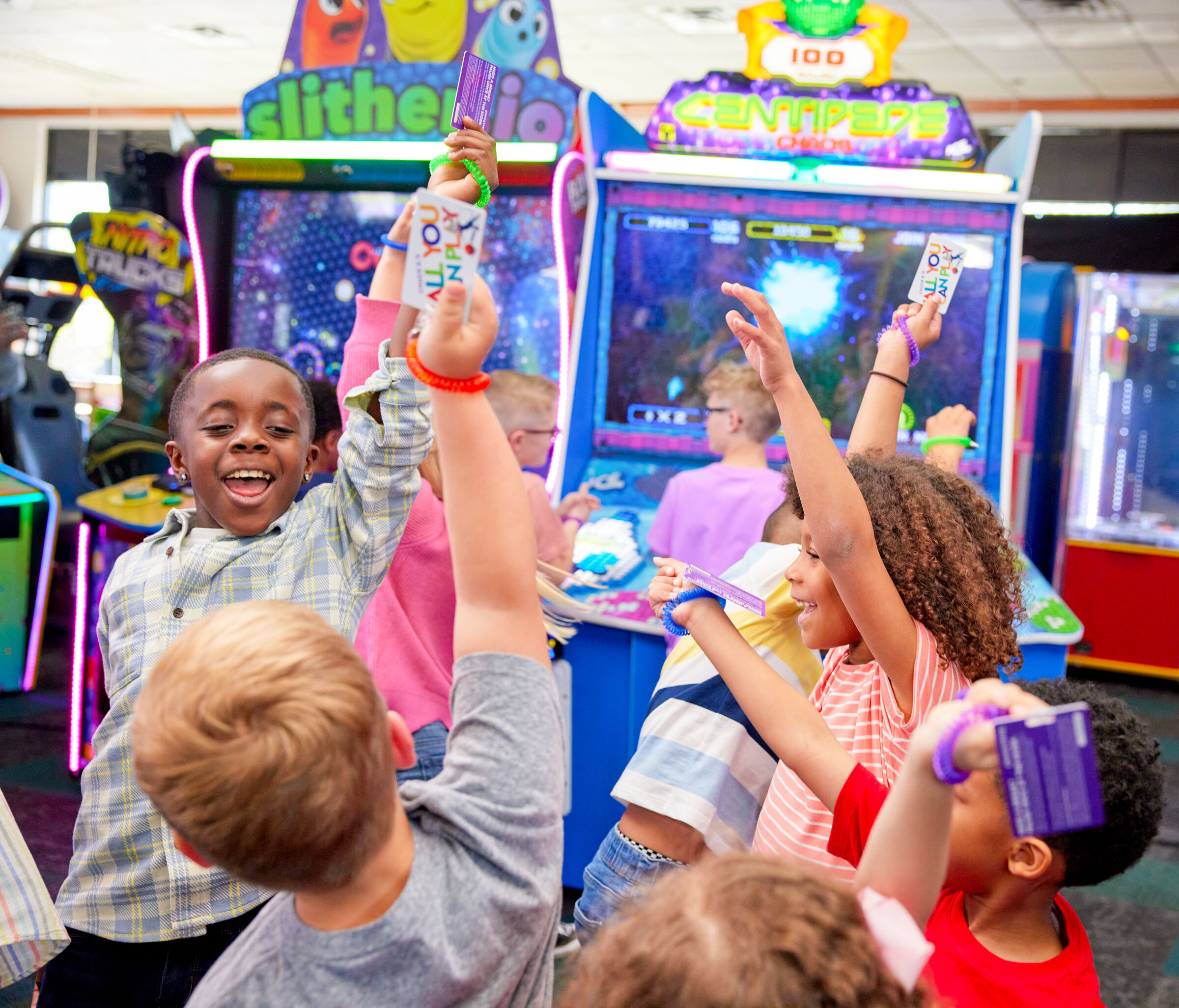 Kids at a Chuck E. Cheese birthday party celebrate with game tickets, smiling near arcade games.