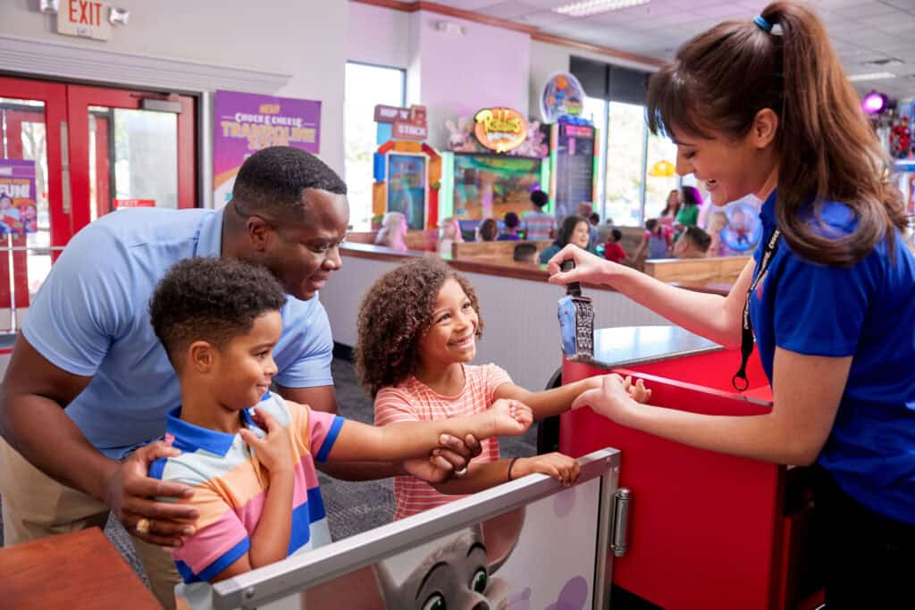 Chuck E. Cheese team member stamping two kids for entry while their parents look on