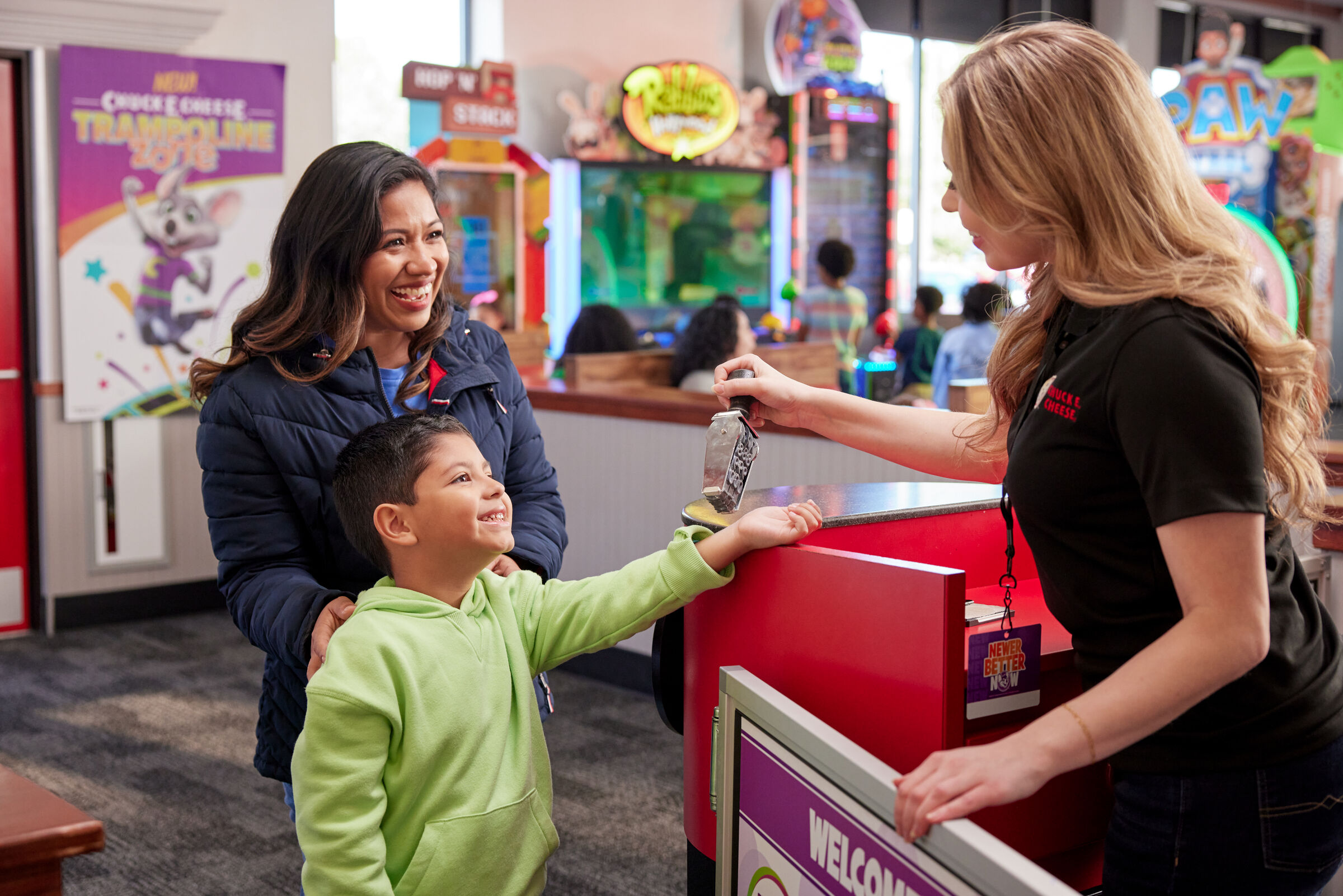 A mother and son check in at Chuck E. Cheese as a team member applies a Fun Pass wristband