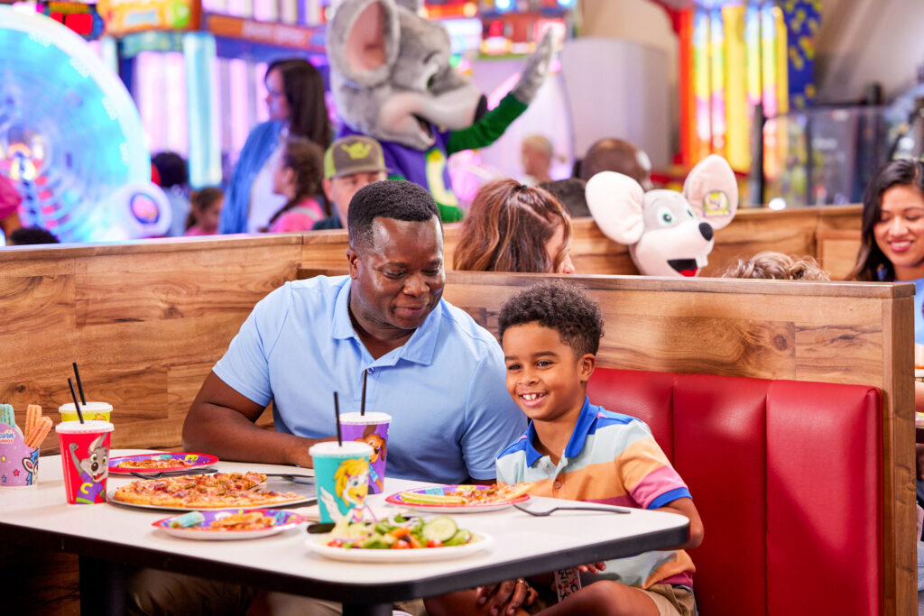 Parent and young child sharing pizza at a table inside Chuck&nbsp;E.&nbsp;Cheese