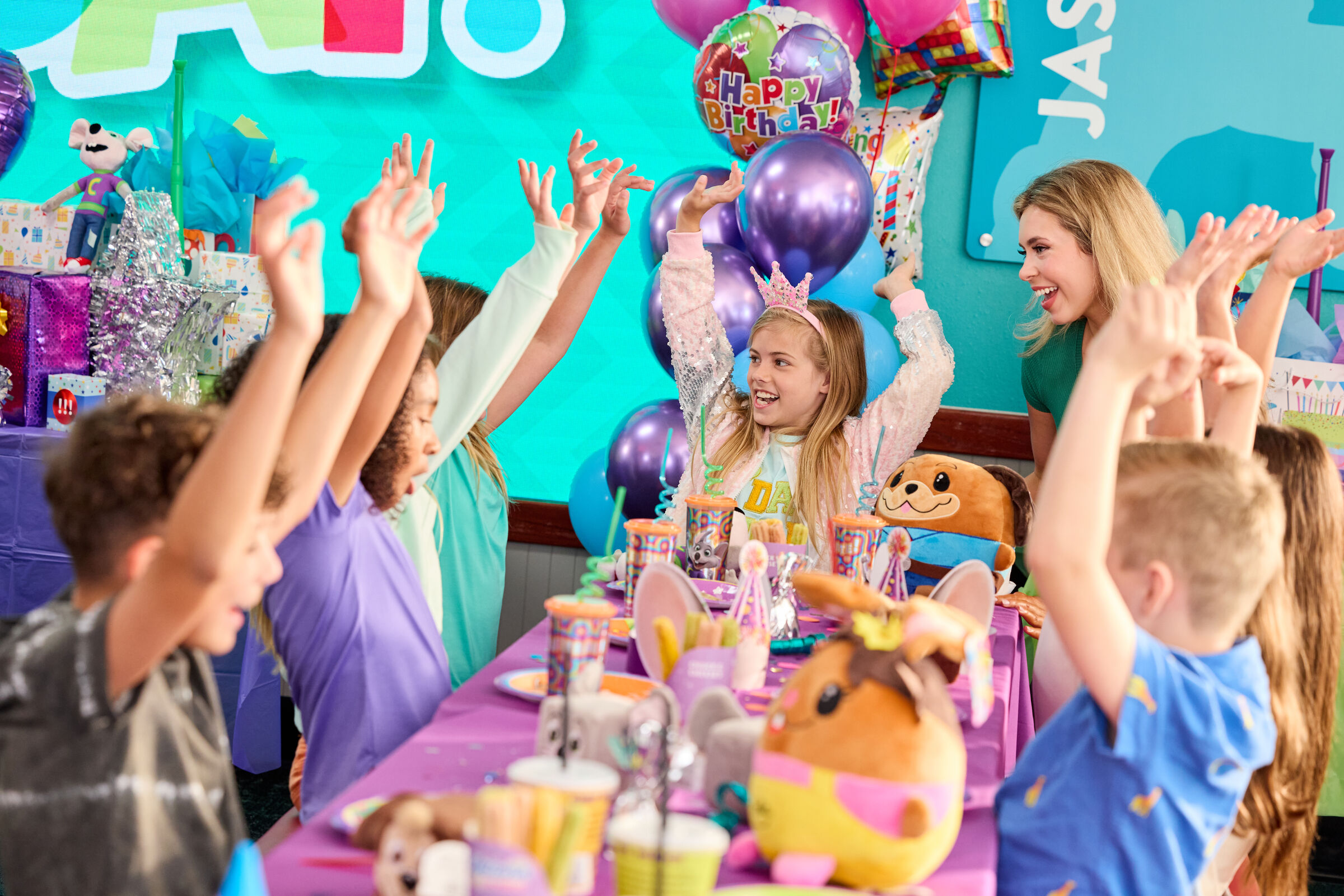 Kids celebrate a birthday at Chuck E. Cheese with plush toys, party supplies, pizza, and arcade games.