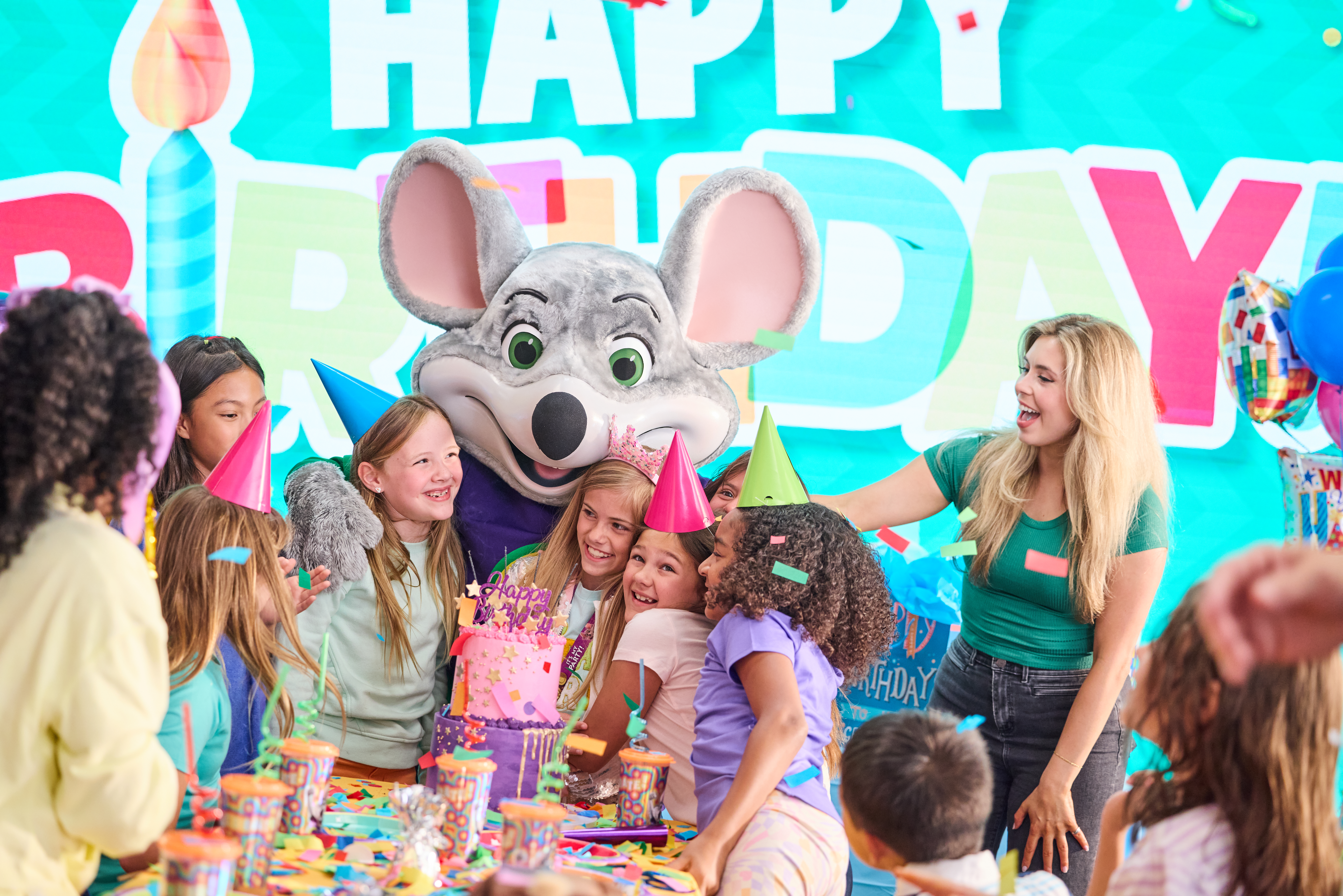 Birthday party celebration at Chuck E. Cheese, kids and family gathered at the party table with decorations and arcade games nearby.