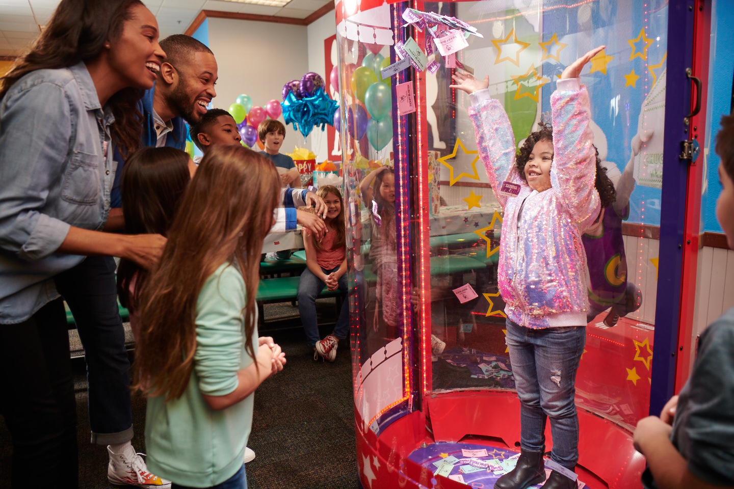 Young child plays Ticket Blaster in Chuck E. Cheese party room as kids and adults cheer during a birthday celebration.
