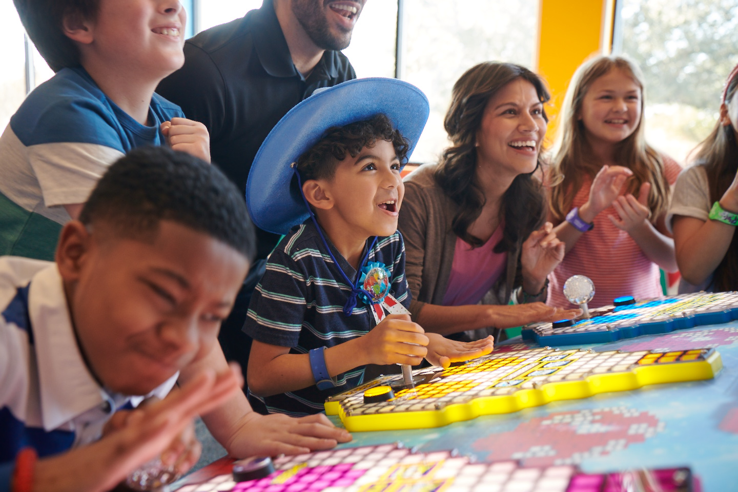 Kids and adults play arcade games together in the Chuck E. Cheese arcade, smiling as a group