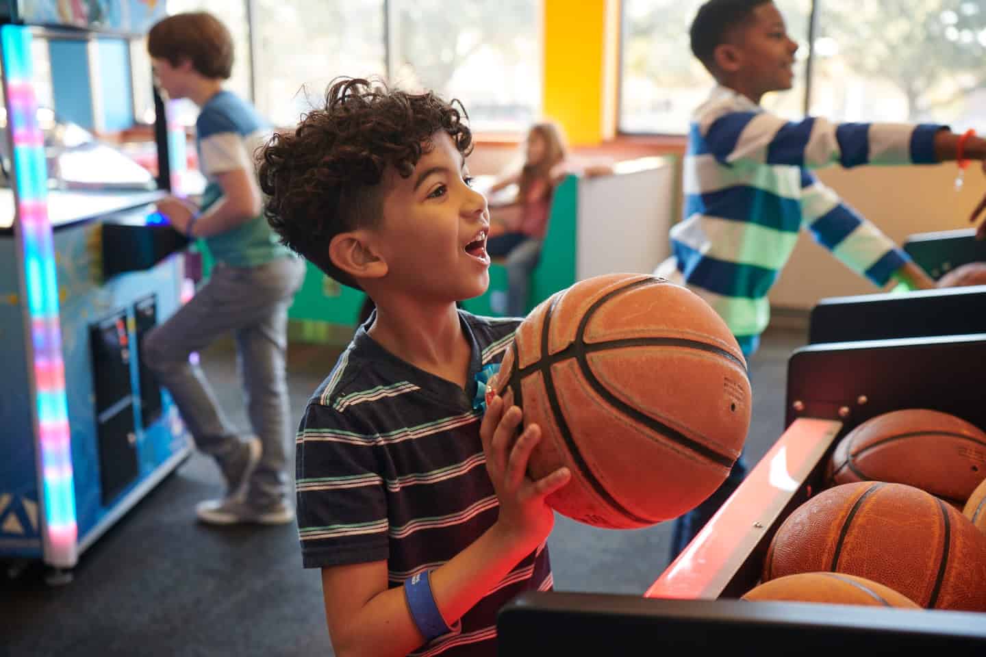 A smiling boy, about 8, holds a basketball at an arcade basketball game in Chuck E. Cheese family fun center.