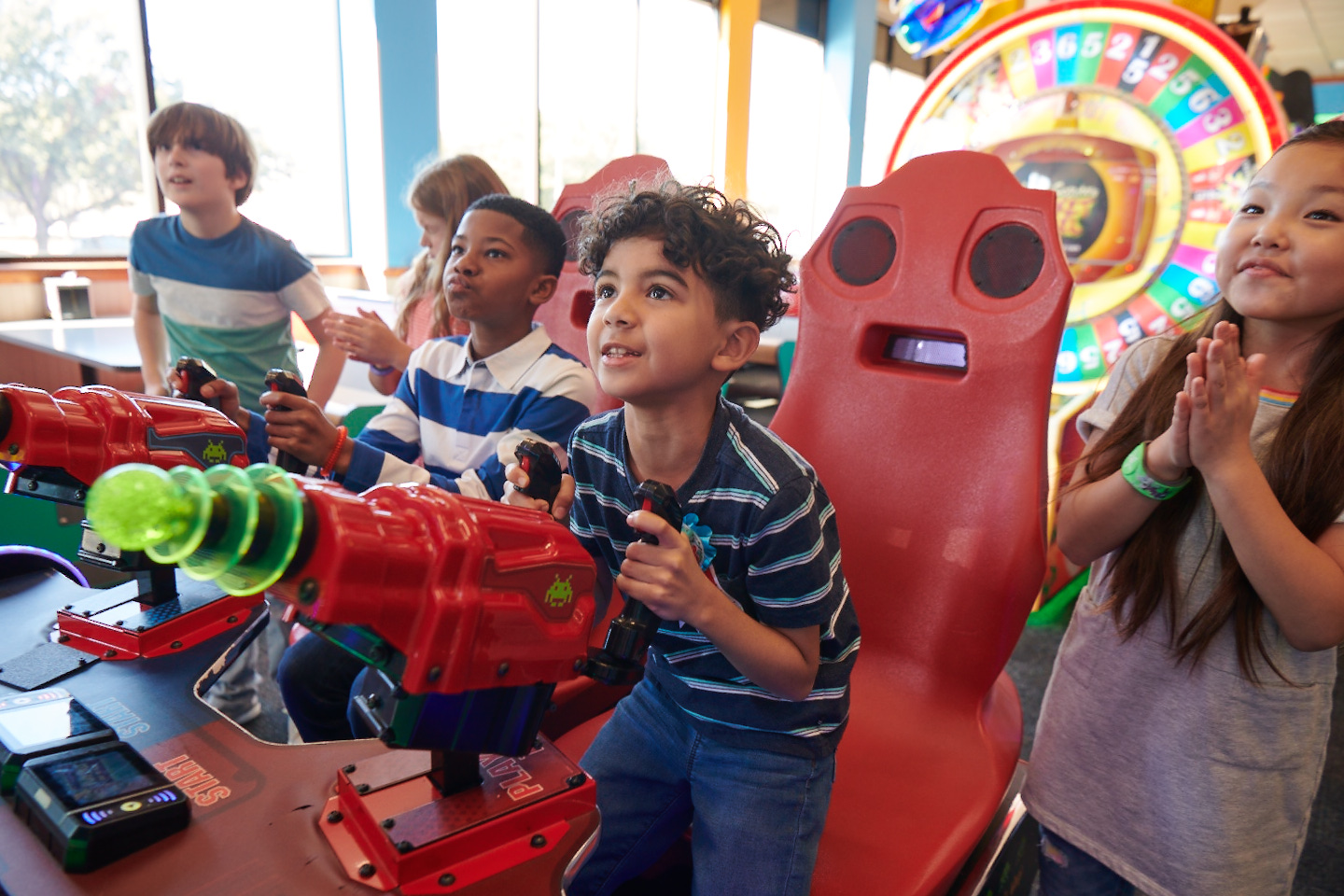 Arcade area at Chuck E. Cheese with kids ages 6–10 playing an arcade game, Fun Pass cards visible.