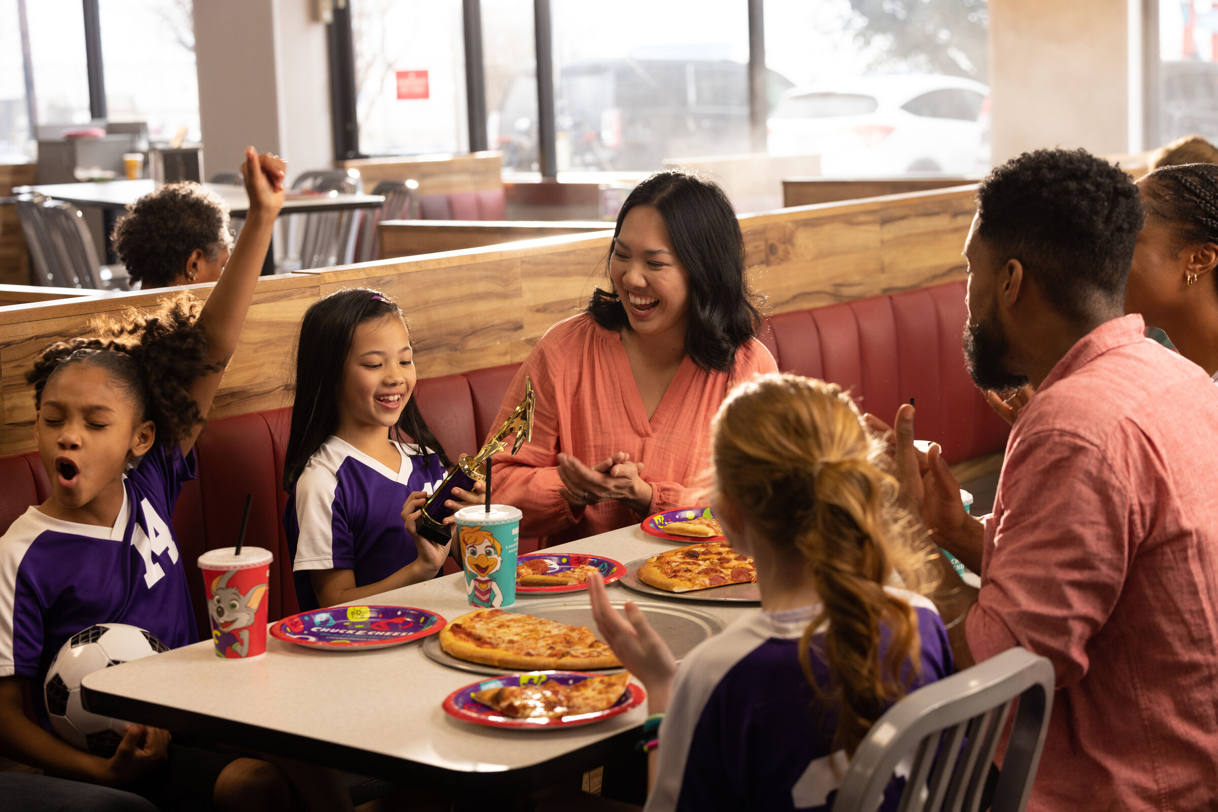 Kids in purple soccer jerseys celebrate with adults at a Chuck E. Cheese team party