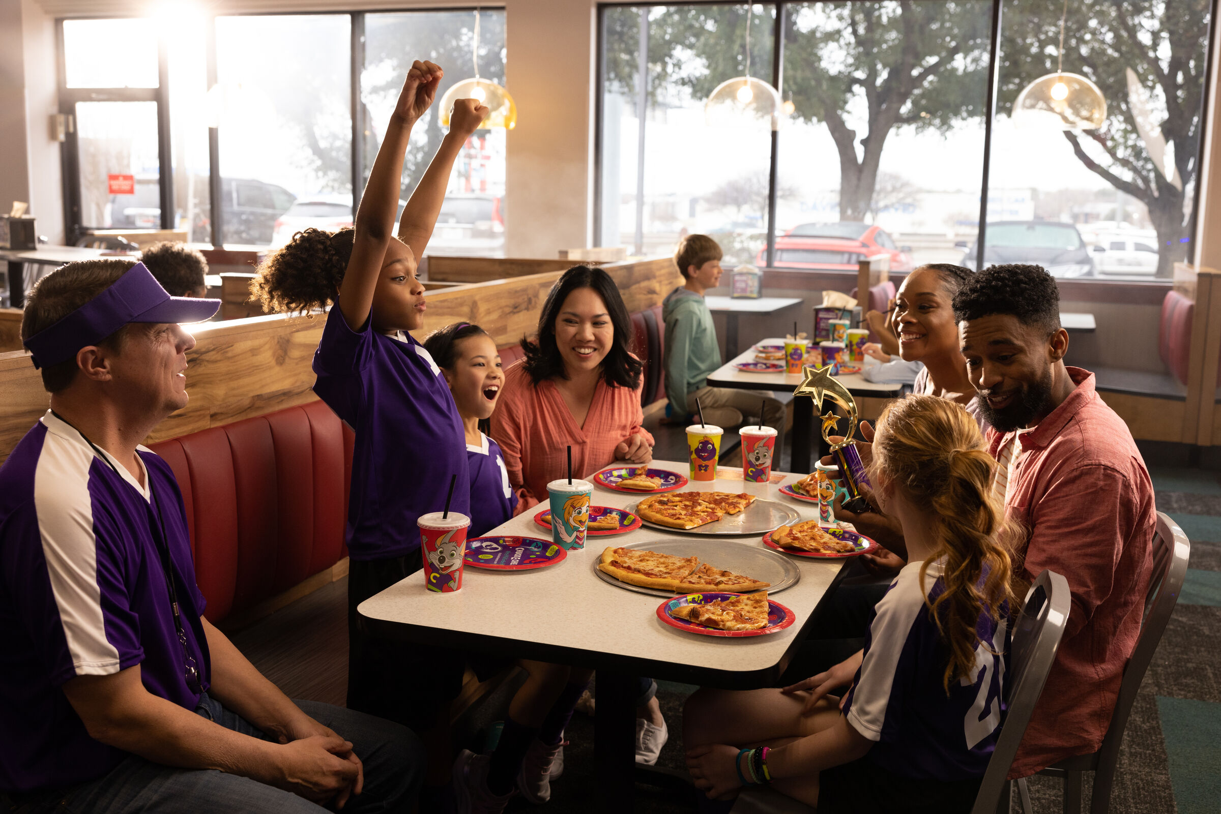 Kids in sports uniforms celebrate at Chuck E. Cheese with pizza and a trophy