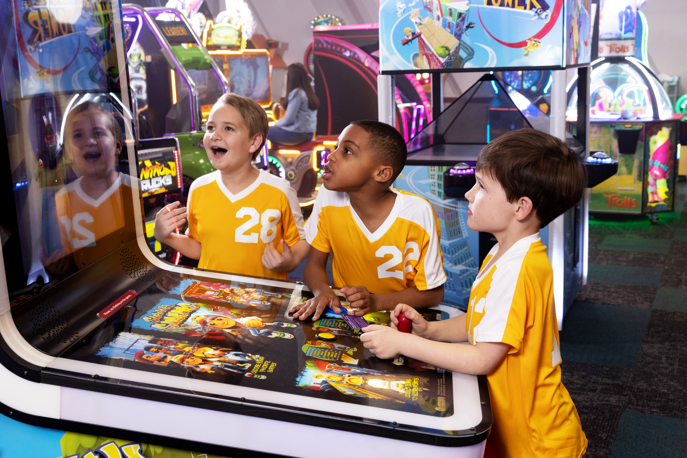 Three boys in yellow sports jerseys play arcade games at Chuck E. Cheese after a team victory