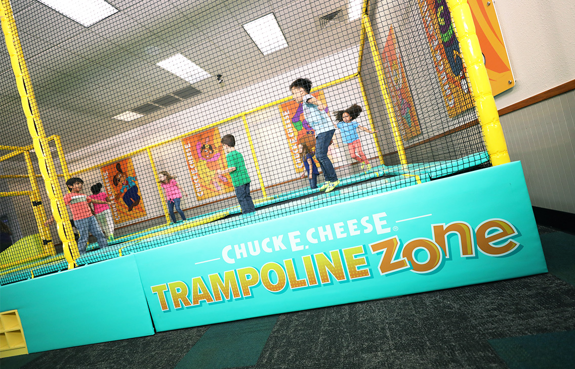 Kids jump on a trampoline at Chuck E. Cheese family fun center, near arcade games and murals.
