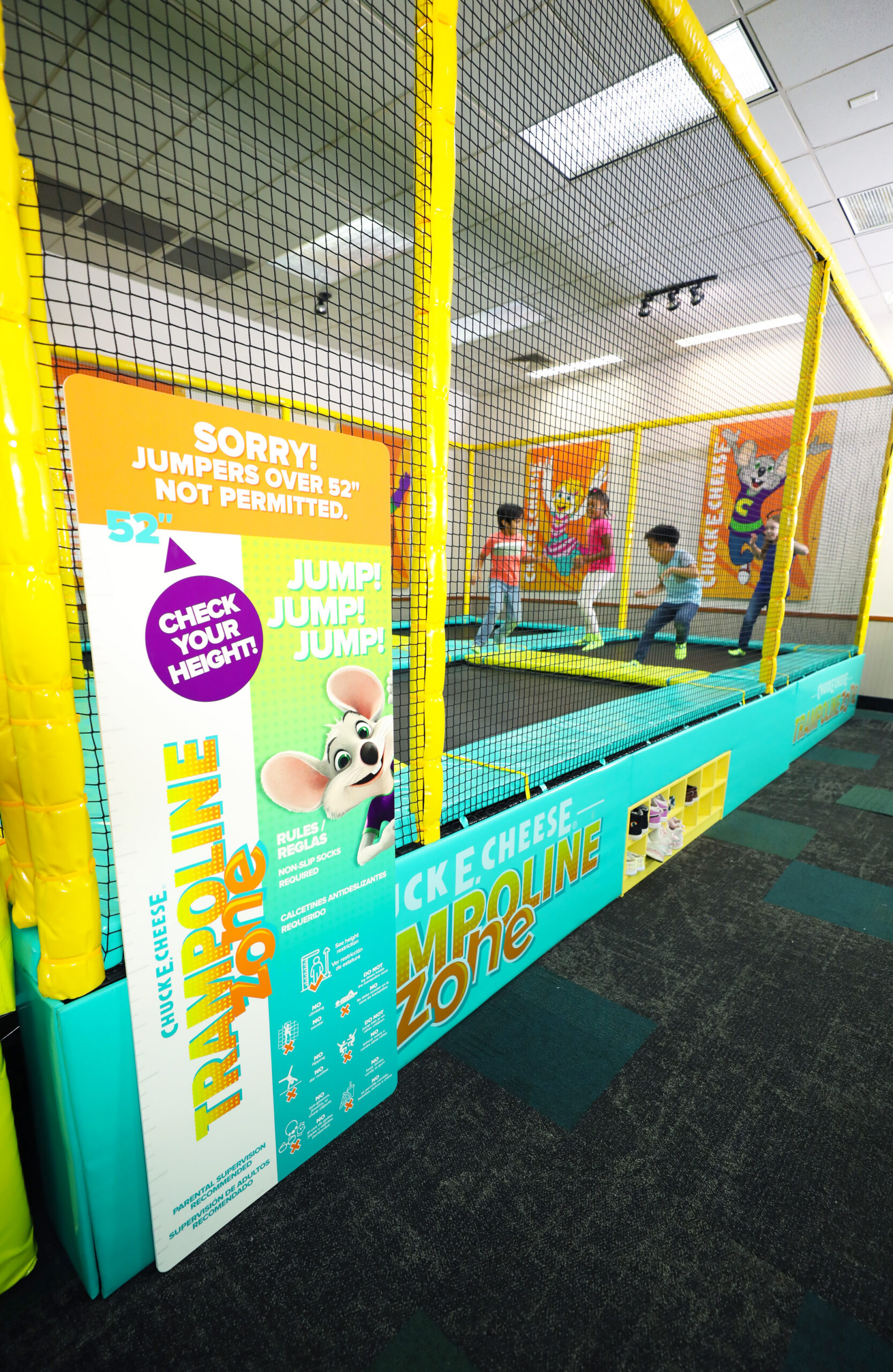 Kids jump in a netted Trampoline Zone at Chuck&nbsp;E.&nbsp;Cheese, with height rules posted and branding visible nearby.