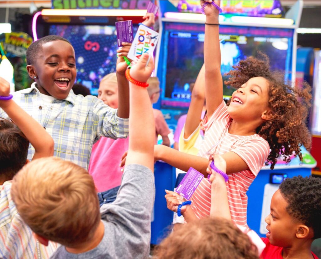 Kids at Chuck E. Cheese birthday party celebrate with tickets and prizes, surrounded by arcade games and pizza, using their Fun Pass.