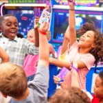 Kids at Chuck E. Cheese birthday party celebrate with tickets and prizes, surrounded by arcade games and pizza, using their Fun Pass.