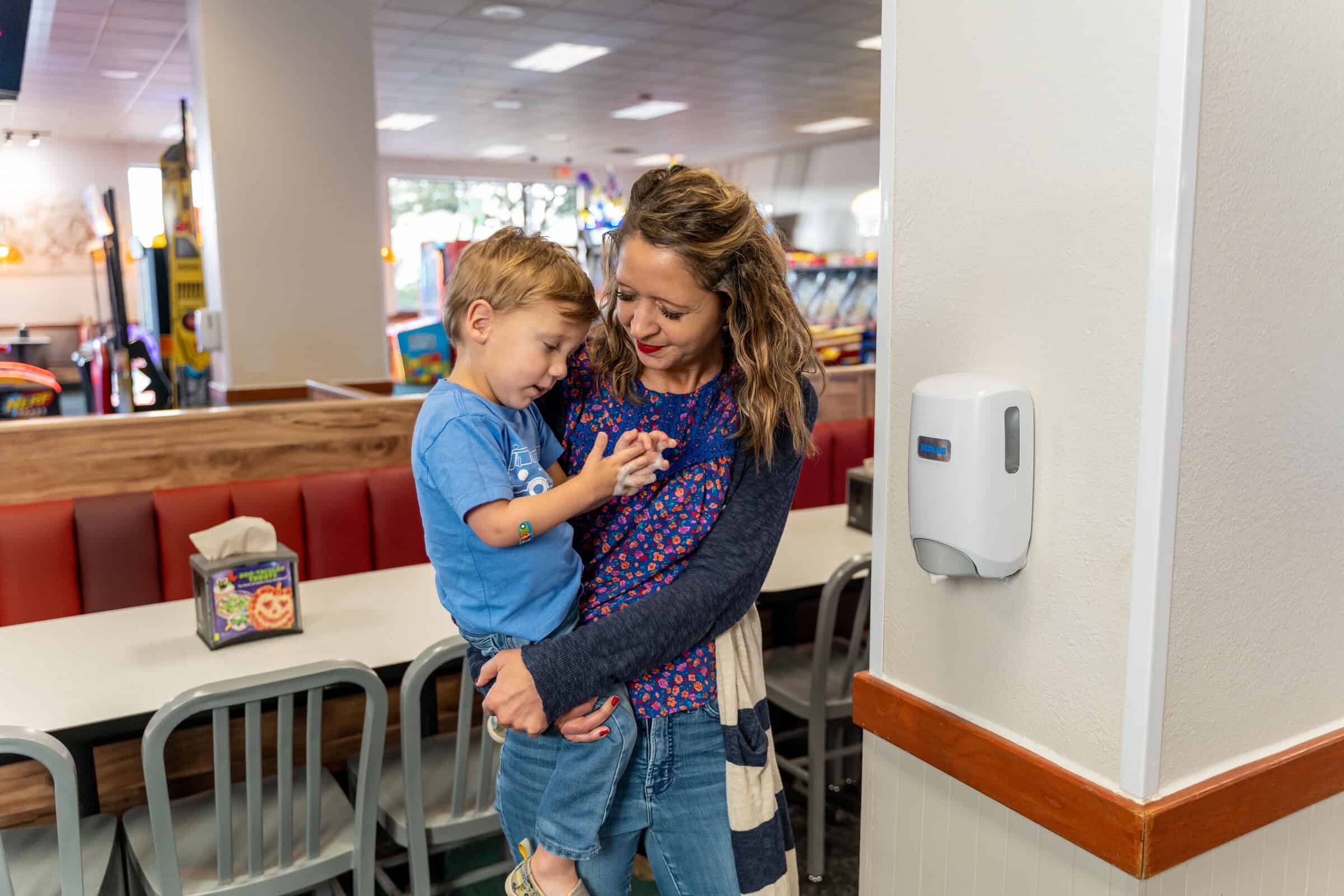 A woman holds a young boy at Chuck E. Cheese near the arcade games.
