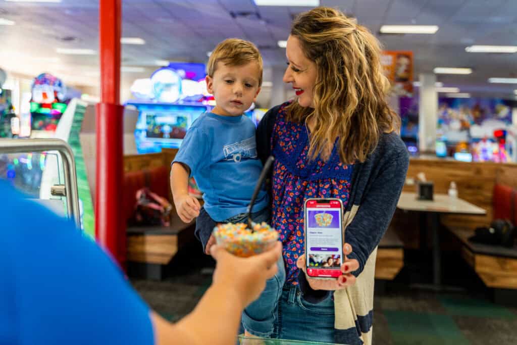 A mom and young son use a Fun Pass as a team member hands them ice cream at Chuck E. Cheese.