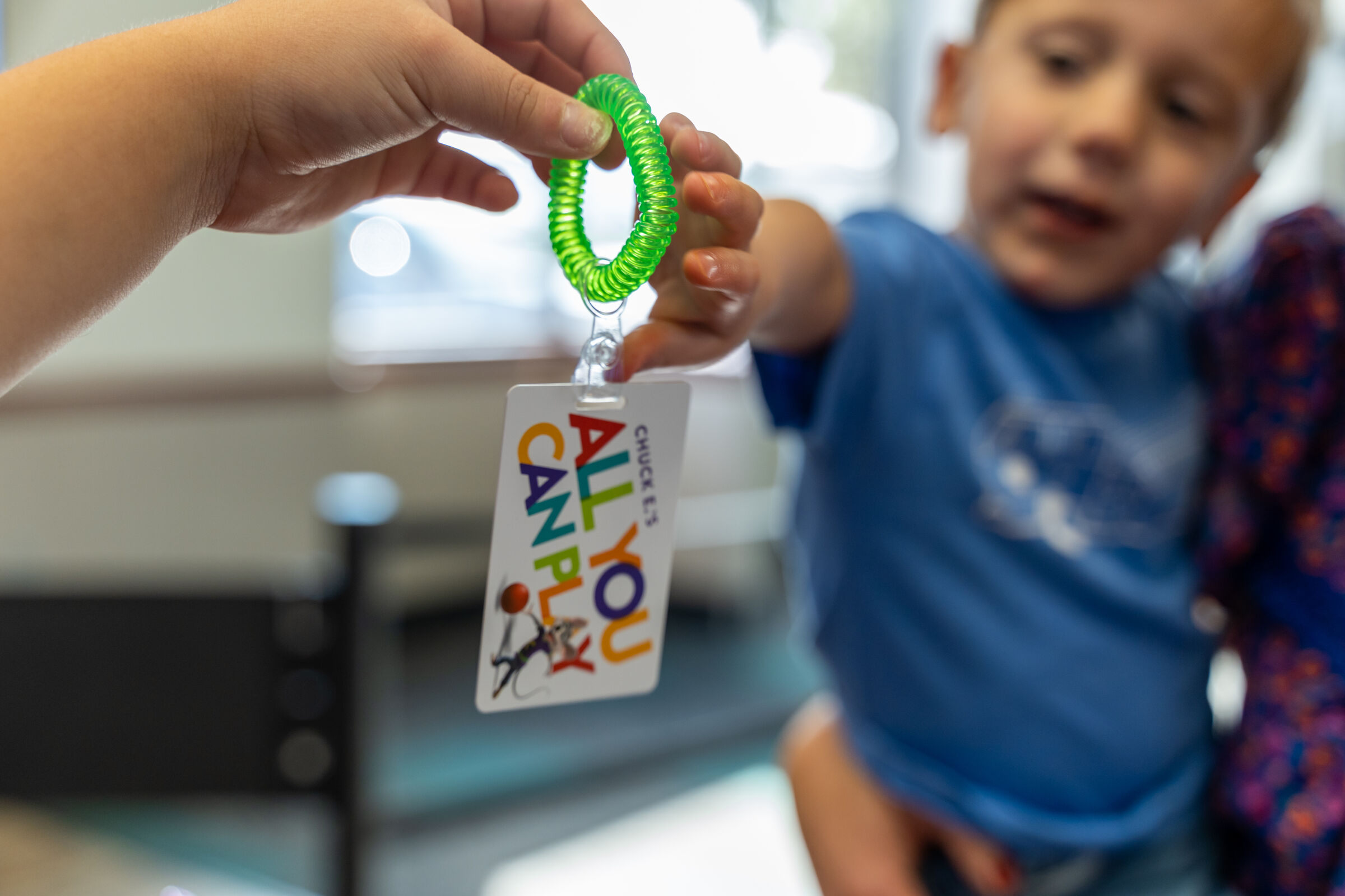 A Chuck&nbsp;E.&nbsp;Cheese staffer hands a green Fun&nbsp;Pass wristband to a young child at a kids' birthday party.