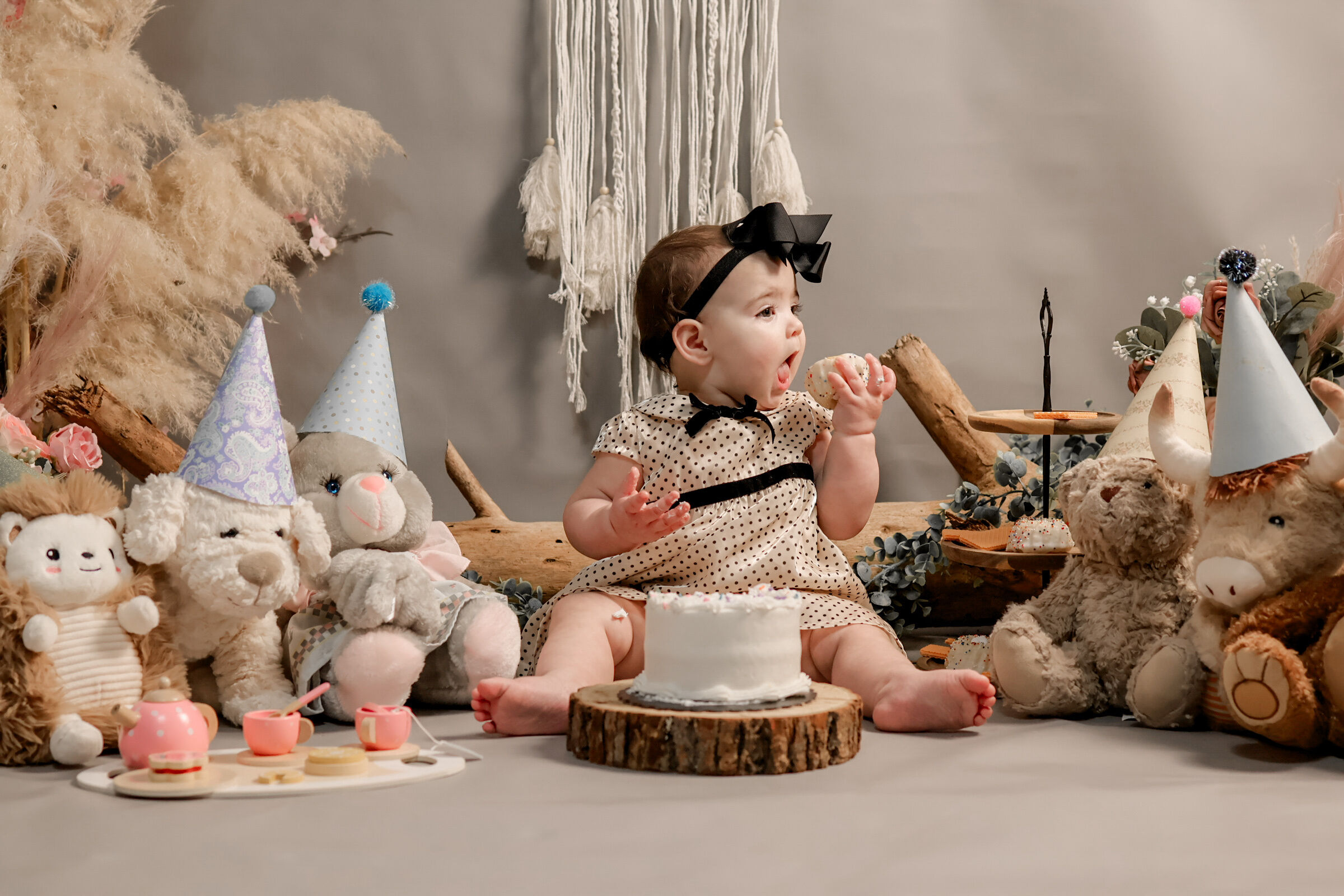 Toddler enjoys a slice of cake on a Chuck&nbsp;E.&nbsp;Cheese party room floor surrounded by plush toys and party hats.