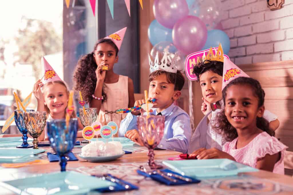 Five kids at a birthday party table with pizza and balloons