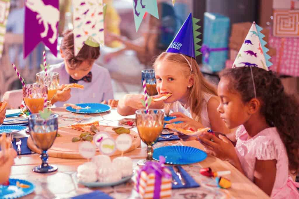 Kids eating pizza at a birthday party table in a Chuck E. Cheese party room