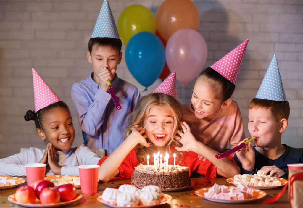 Kids at a Chuck E. Cheese birthday table with a chocolate cake and balloons